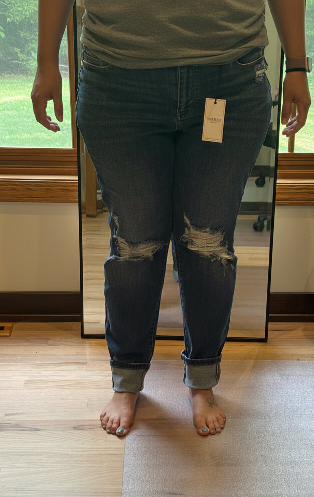 Plus size model wearing Judy Blue mid rise boyfriend jeans in dark wash size 15, front view with knee distressing and cuffed hem
